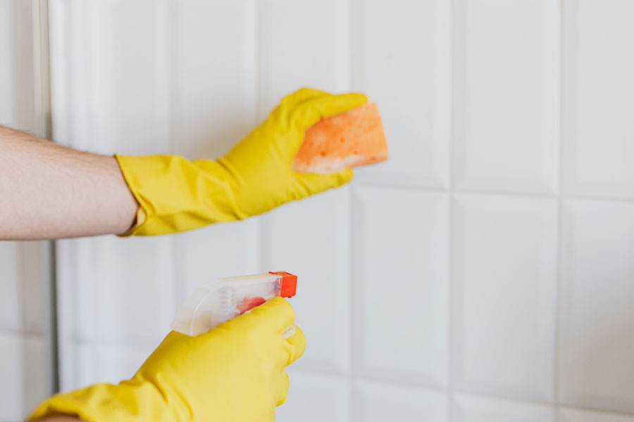 Close up of hands in rubber gloves scrubbing tile, to represent professional home cleaning services in Woodbury, Minnesota